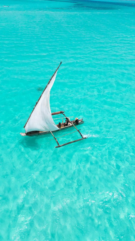 Aerial view of a traditional sailboat on vibrant turquoise waters under a clear summer sky.