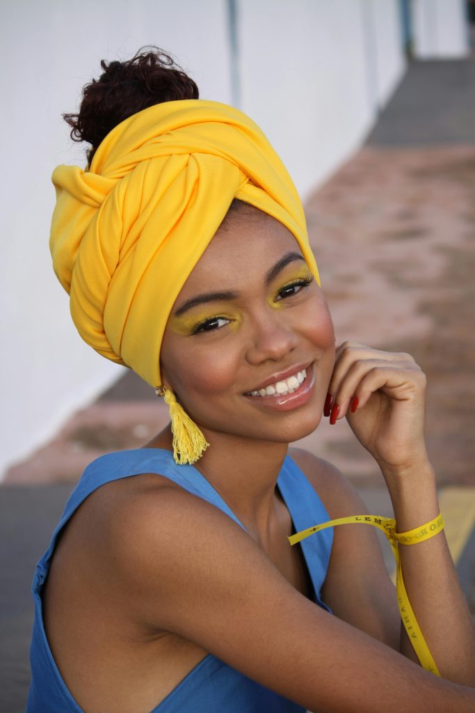 Beautiful woman with a yellow headwrap and blue top, smiling outdoors.