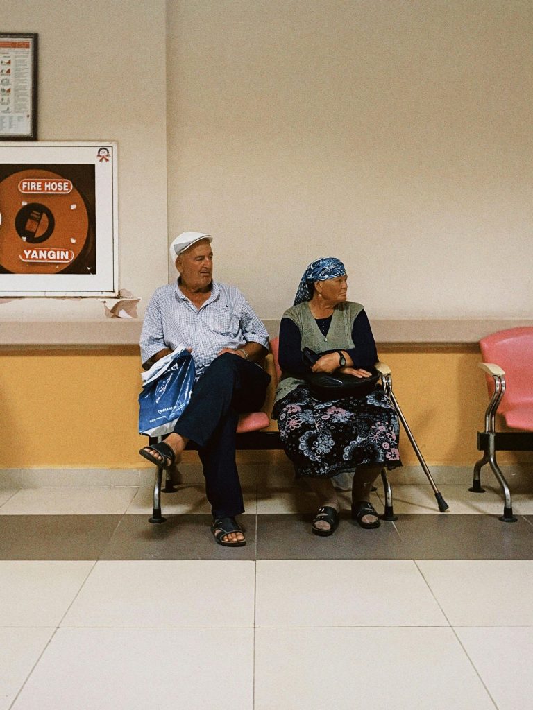 Senior couple sitting in a hospital corridor waiting area, expressing quiet patience.