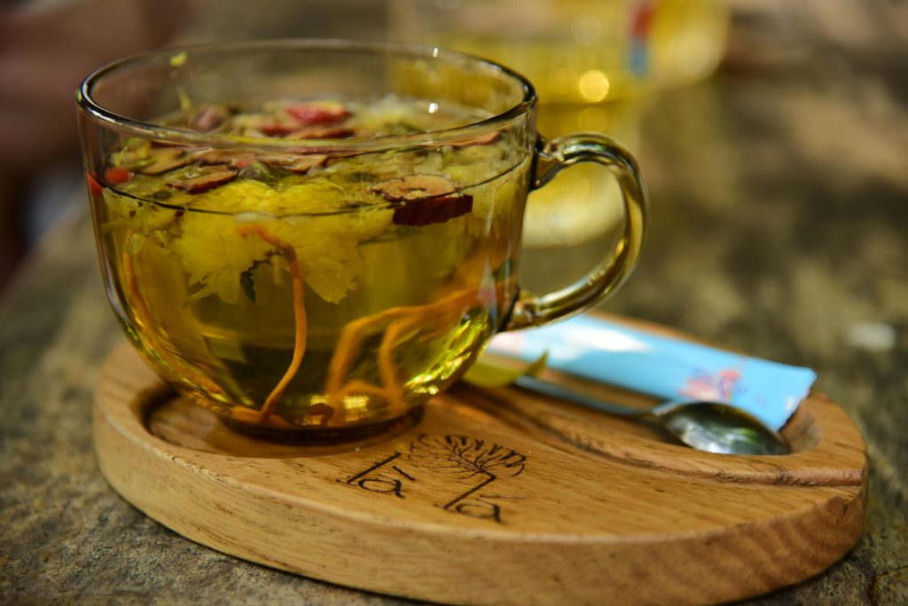 Close up of herbal tea with flowers in a glass cup on a wooden tray. Perfect for relaxing.