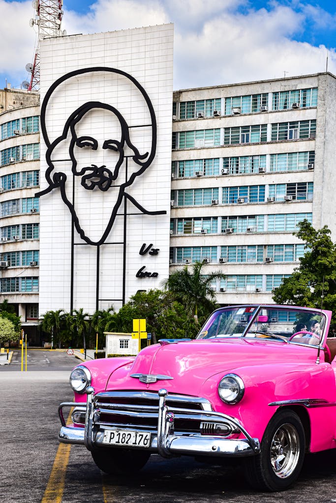 Classic pink car in Havana, Cuba against a mural backdrop, capturing the city's vibrant spirit.