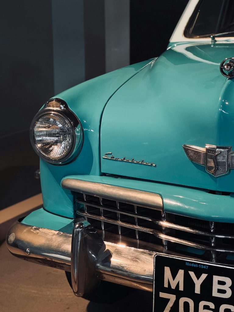 Close-up of the front of a vintage turquoise car with a classic design, showcasing headlight and chrome details.