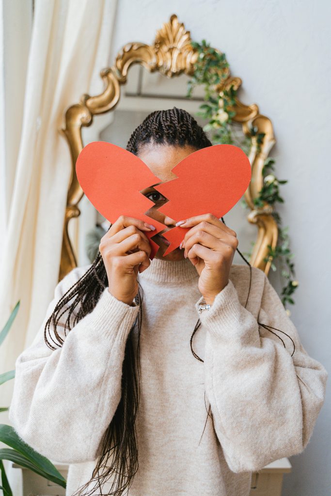 An adult woman holding a broken heart paper in front of a mirror, symbolizing heartbreak.