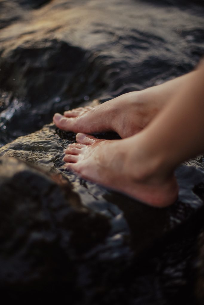 Close-up of bare feet on wet, dark rocks during twilight, capturing serene outdoor nature.