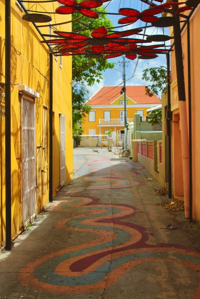 Vibrant alley in Willemstad with colorful street art and tropical architecture.
