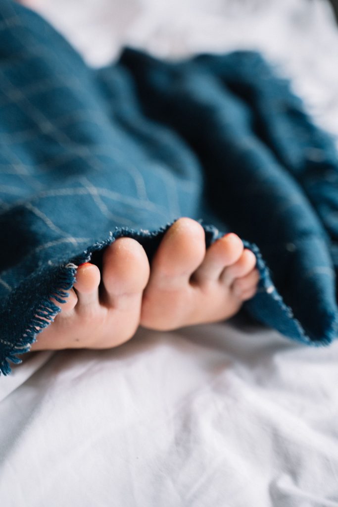 Cozy feet tucked under a warm blue blanket on a soft bed, creating comfort vibes.