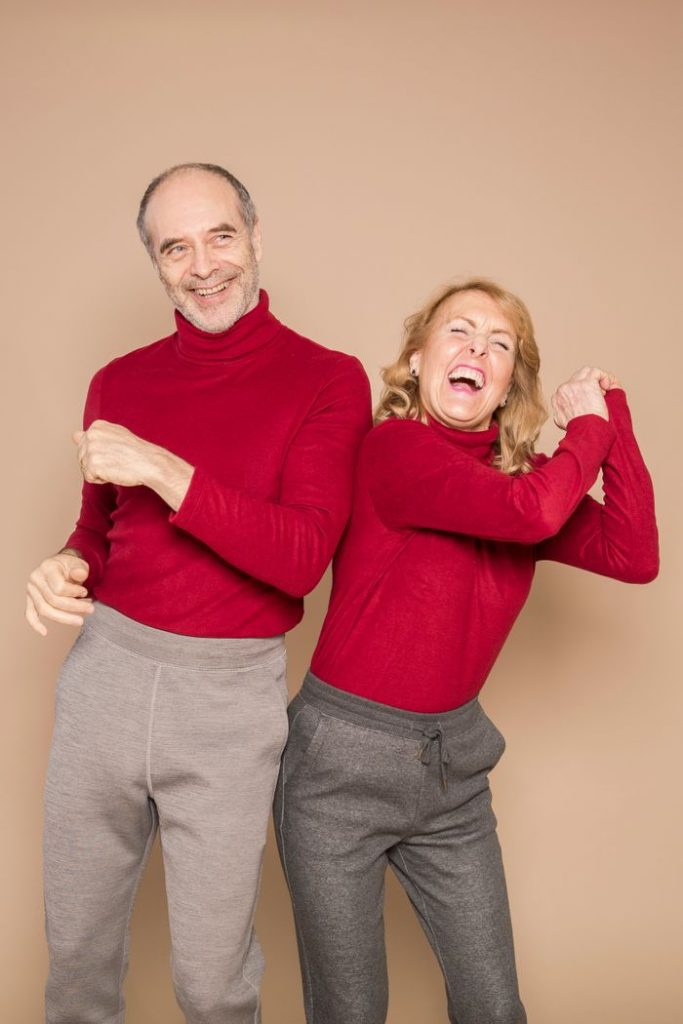 A happy senior couple dancing and laughing in red sweaters against a neutral background.