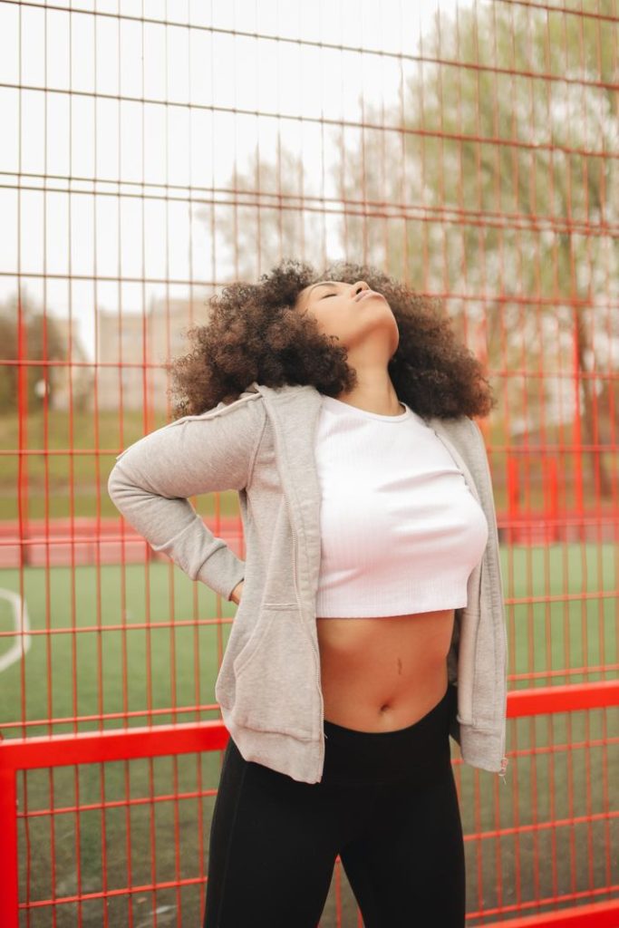 A young black woman in athletic wear stretching at an outdoor sports facility.