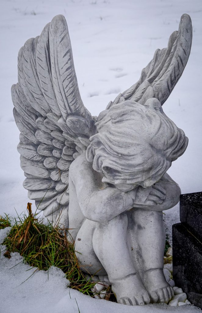 A peaceful angel figurine with wings seated in snow, evoking serenity and contemplation.