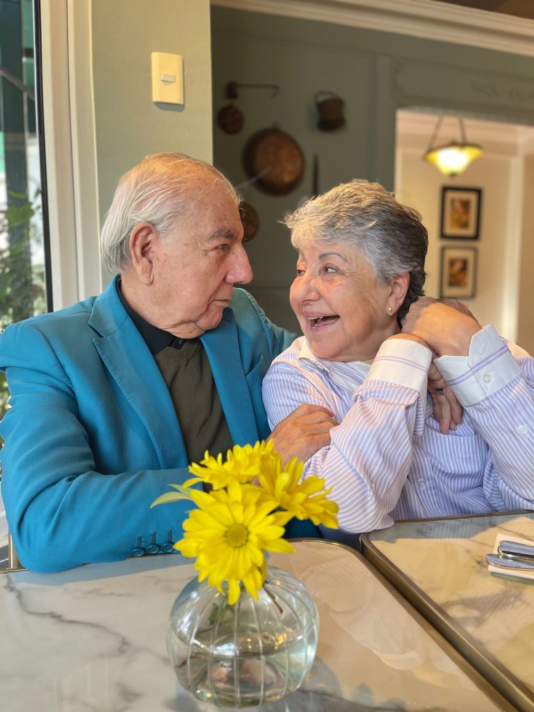 A senior couple sharing a joyful moment at a table indoors, surrounded by warm decor.