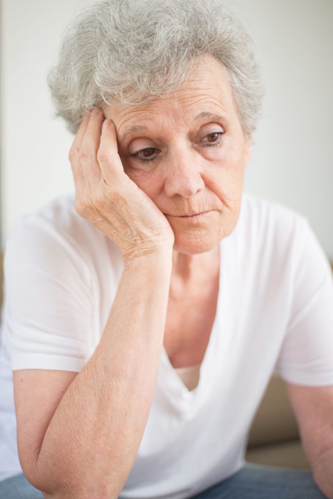 A senior woman with a contemplative expression, indoors.