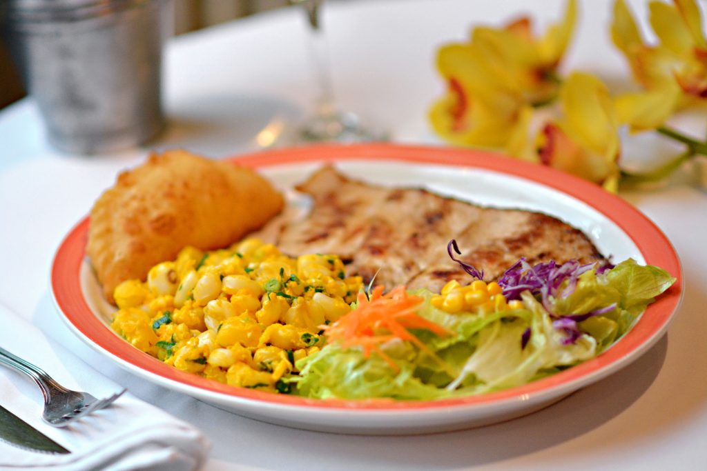 Mouth-watering grilled chicken with corn, salad, and empanada on a plate.