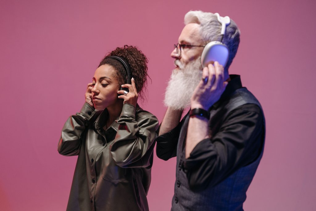 Man and woman listening to music on headphones against a pink background.